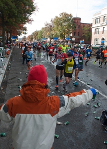 A volunteer hands out cups of water as a wave of runners passes by in the 2013 New York City Marathon.